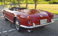 an old red sports car parked in a parking lot