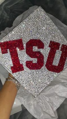 someone is holding up a graduation cap with the word tsu on it in red and silver sequins