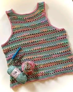 a crocheted tank top with yarn and balls of yarn on the bottom, next to a ball of thread