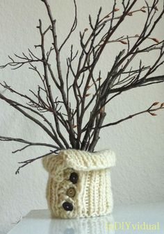 a knitted planter with branches in it and a button on the front side