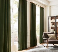 a living room with green curtains and a chair in front of a bookcase filled with books