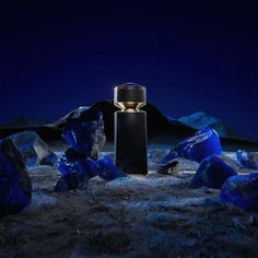 an illuminated bottle sitting in the middle of some rocks and ice crystals at night with mountains in the background