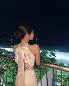 a woman standing on top of a balcony next to a lush green hillside at night