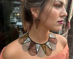 a woman wearing a necklace and earrings on her neck looking away from the camera while standing in front of a brick wall