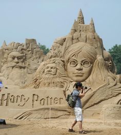 two people taking pictures in front of a sand castle with hogwarts on it