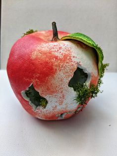 an apple that has been painted red and white with some green leaves on the inside