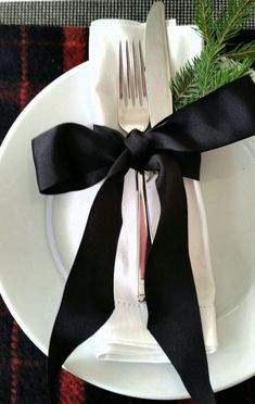 a white plate topped with a fork and knife next to a black ribbon on top of it