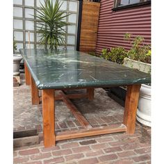 a green table sitting on top of a brick floor next to a potted plant