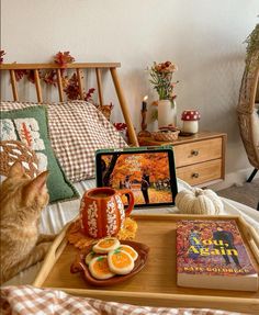 a cat sitting on a bed looking at an orange book and coffee cup next to it