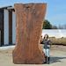 a person standing next to a large piece of wood on the ground near a building