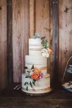 a three tiered cake with flowers on top is sitting on a table next to a wooden wall