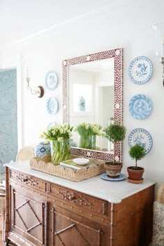 a wooden dresser topped with vases filled with flowers next to a wall mounted mirror