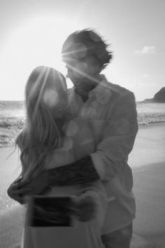 black and white photograph of a couple embracing on the beach with sun shining through them