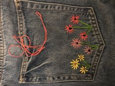 the back pocket of a pair of jeans with flowers embroidered on it and string attached to them