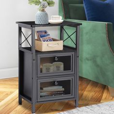 a small end table with two drawers and a basket on the top, in front of a green couch