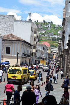 many people are walking down the street in front of cars and buildings, some with yellow cabs