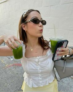 a woman is holding a green drink and looking at her cell phone