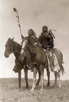 an old photo of two native american men on horses in the desert, one holding a spear