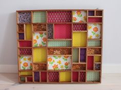 a multicolored patchwork wooden box with flowers and dots on the sides, sitting against a white wall