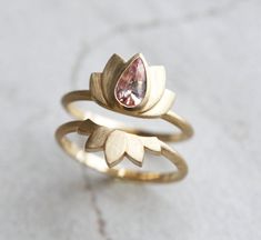 A part of our Zen collection, comes the second design with peach sapphire and brushed yellow gold setting, the Lotus ring. The lotus flower is one of the most ancient and deepest symbols of our planet. The lotus flower grows in muddy water and rises above the surface to bloom with remarkable beauty. Untouched by the impurity, lotus symbolizes the purity of heart and mind. The lotus flower represents long life, health, honor and good luck. This ring and ring set is original design patented Capuci Pear Sapphire Ring, Unique Sapphire Rings, Sapphire Wedding Ring Set, Peach Sapphire Rings, Diamond Alternative Engagement Ring, Peach Sapphire Engagement Ring, Sapphire Engagement Ring Set, Lotus Ring, Pink Engagement Ring