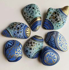 six painted rocks arranged in a circle on a white surface with gold and blue designs