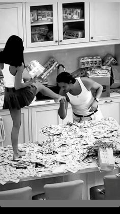 two women standing on top of a kitchen counter next to a table covered in papers