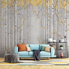 a blue couch sitting in front of a wall with yellow leaves on it and a tree mural