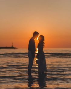 a couple kissing in the ocean at sunset