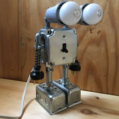 a metal robot with two white lights on it's head sitting on a wooden table