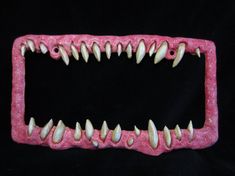 a pink frame with white teeth and long spikes on the front, against a black background