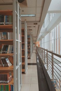 an empty library filled with lots of books next to tall glass windows and wooden shelves