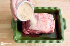 a person pouring seasoning into a piece of meat on a green plate with a white bowl