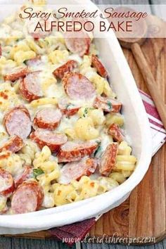 a casserole dish with sausage and pasta in it on a wooden cutting board