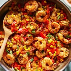 a skillet filled with shrimp, corn and tomato salad next to a wooden spoon