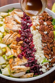 someone pouring dressing into a salad with chicken, apples, cranberries and pecans