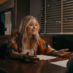 a woman sitting at a table with her hands out in front of the person who is talking