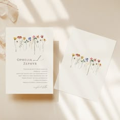 a wedding card with flowers on it next to some glasses and a flower bouquet in the background