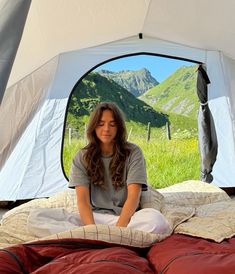 a woman sitting in a tent on top of a bed with mountains in the background