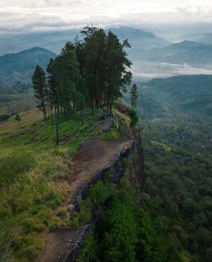 a dirt road on the side of a mountain with trees and mountains in the background