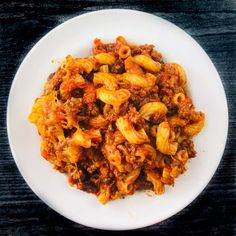 a white plate topped with pasta covered in meat and sauce on top of a wooden table