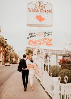 a man and woman walking down the sidewalk in front of a white chapel