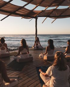 a group of women sitting on top of a wooden floor in front of the ocean