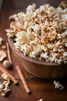 a wooden bowl filled with popcorn next to cinnamon sticks