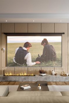 two people sitting in front of a large screen tv on a wall above a fireplace