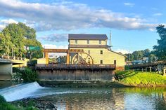 an old mill on the side of a river with a bridge in the foreground