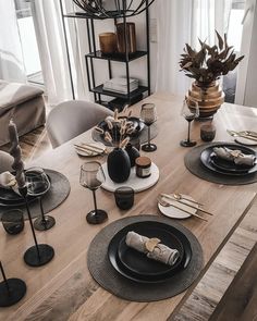 a wooden table topped with black plates and place settings