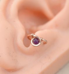 an earring with a purple stone in it sitting on top of a piece of plastic