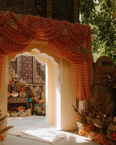 an archway is decorated with red and orange fabric for the entrance to a garden area