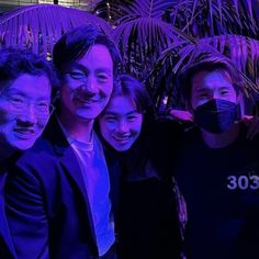 three men and two women pose for a photo in front of palm trees wearing face masks