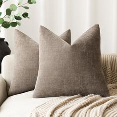 two pillows sitting on top of a couch next to a vase filled with green leaves